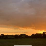 Picture taken summer 2020 of the glaring sunset over the murkier, darker fields.