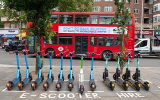 E-scooters lined up across from a red London bus. Credit: PA